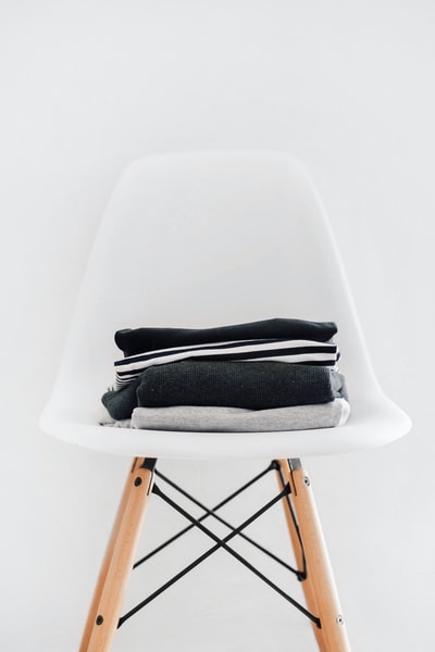 黑色、白色和灰色织物堆在棕色框架的白色软垫椅子上